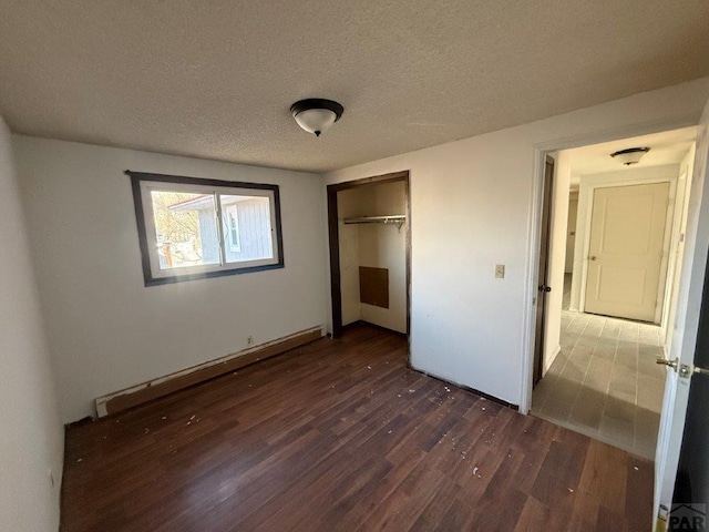 unfurnished bedroom with a baseboard radiator, a closet, dark wood finished floors, and a textured ceiling
