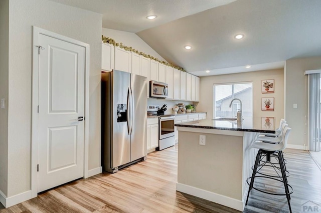 kitchen with appliances with stainless steel finishes, a kitchen island with sink, vaulted ceiling, a kitchen bar, and a sink