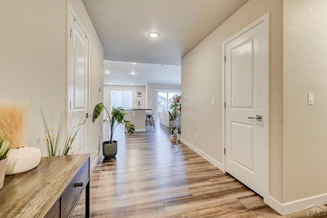 hall featuring light wood-style floors, baseboards, and recessed lighting