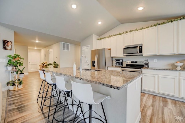 kitchen featuring stainless steel appliances, a sink, visible vents, white cabinets, and a kitchen bar