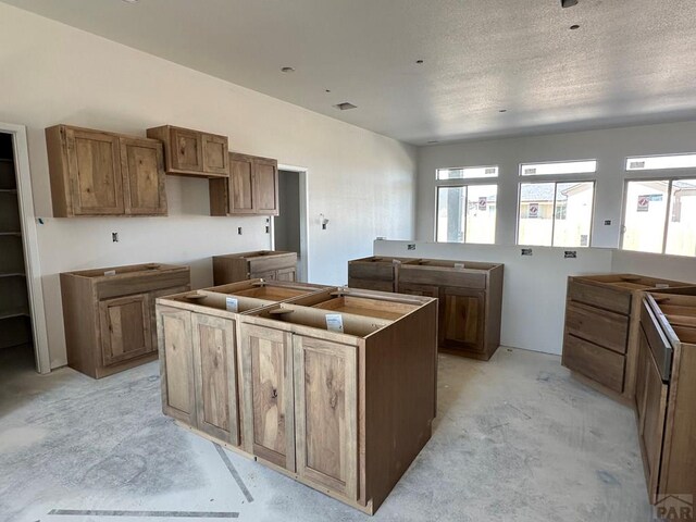 5400 Darter Ct, Pueblo, CO 81008 - kitchen with unfinished concrete floors, a kitchen island, brown cabinets, and a textured ceiling
