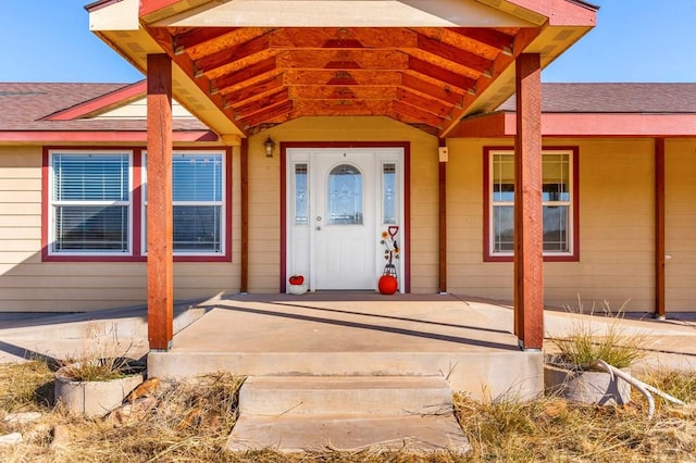 doorway to property featuring covered porch and a shingled roof