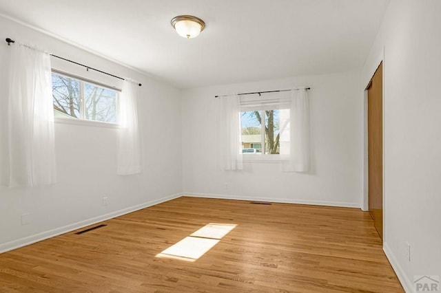 empty room featuring visible vents, light wood-style flooring, and baseboards