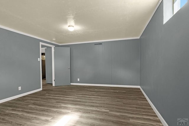 empty room featuring crown molding, wood finished floors, visible vents, and baseboards