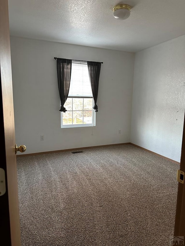 empty room with a textured ceiling, carpet floors, visible vents, and baseboards