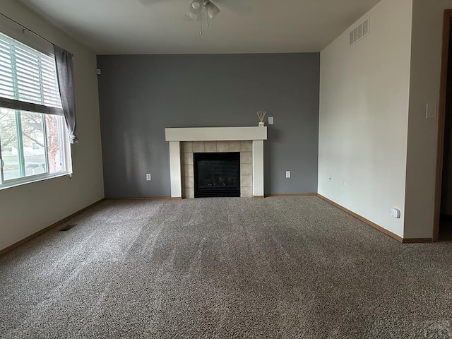 unfurnished living room with carpet floors, visible vents, ceiling fan, a tile fireplace, and baseboards