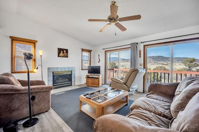 living area featuring ceiling fan, a fireplace, vaulted ceiling, and wood finished floors