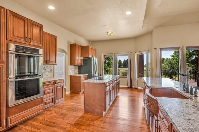 368 S Camino De Los Ranchos, Pueblo West, CO 81007 - kitchen featuring stainless steel appliances, decorative backsplash, light stone countertops, brown cabinets, and light wood-style floors