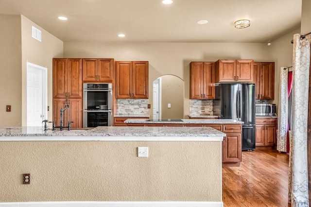 368 S Camino De Los Ranchos, Pueblo West, CO 81007 - kitchen with appliances with stainless steel finishes, a center island with sink, light wood-type flooring, brown cabinetry, and tasteful backsplash