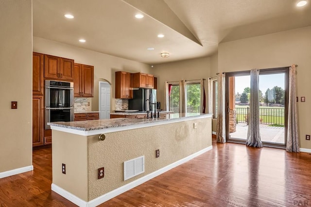 368 S Camino De Los Ranchos, Pueblo West, CO 81007 - kitchen featuring appliances with stainless steel finishes, brown cabinets, a kitchen island with sink, tasteful backsplash, and dark wood-type flooring