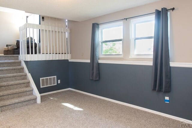 spare room featuring visible vents, baseboards, stairway, carpet, and a textured ceiling