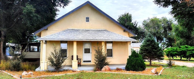 view of front of home with a shingled roof, a front lawn, a porch, and stucco siding