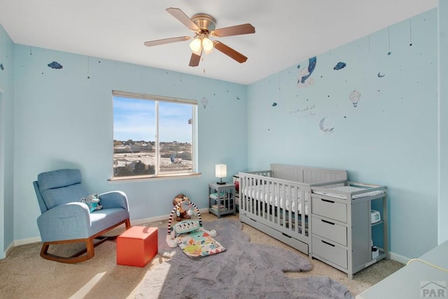 bedroom with light carpet, a nursery area, baseboards, and a ceiling fan