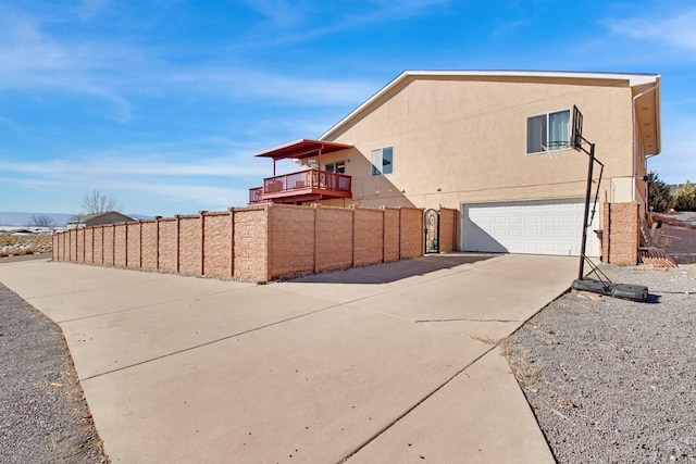 view of side of property with concrete driveway, an attached garage, fence, and stucco siding