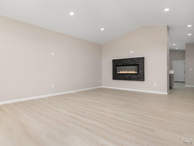 unfurnished living room featuring baseboards, a glass covered fireplace, vaulted ceiling, light wood-type flooring, and recessed lighting