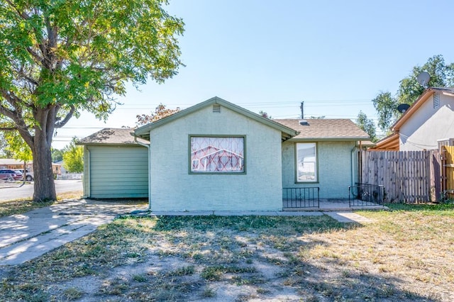 back of house featuring a yard, roof with shingles, fence, and stucco siding