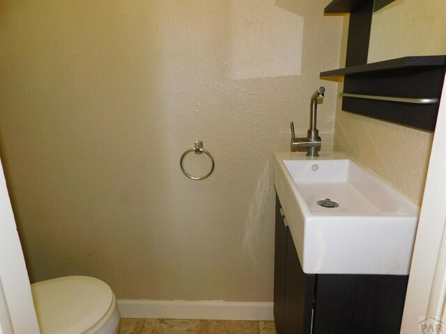 half bath featuring toilet, tile patterned flooring, baseboards, and vanity