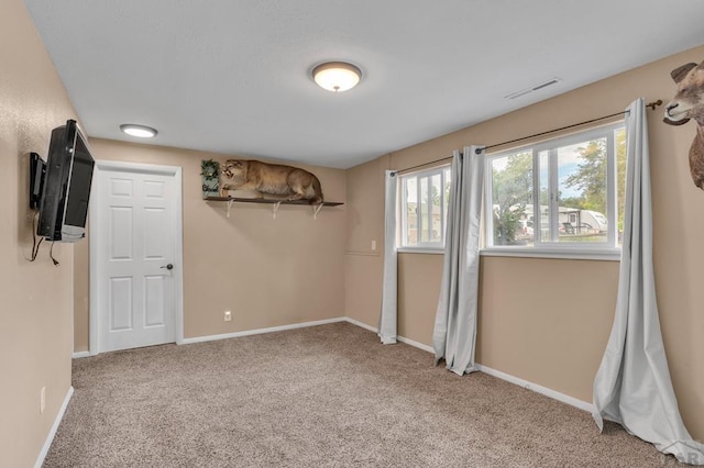 below grade area with baseboards, visible vents, and light colored carpet