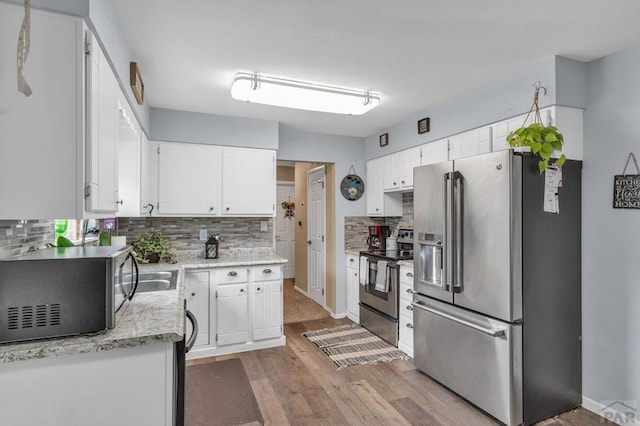 kitchen with light wood finished floors, decorative backsplash, appliances with stainless steel finishes, white cabinets, and baseboards