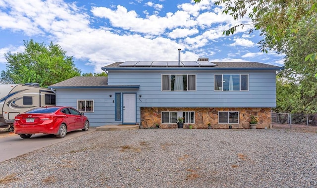 tri-level home with driveway, stone siding, fence, and solar panels