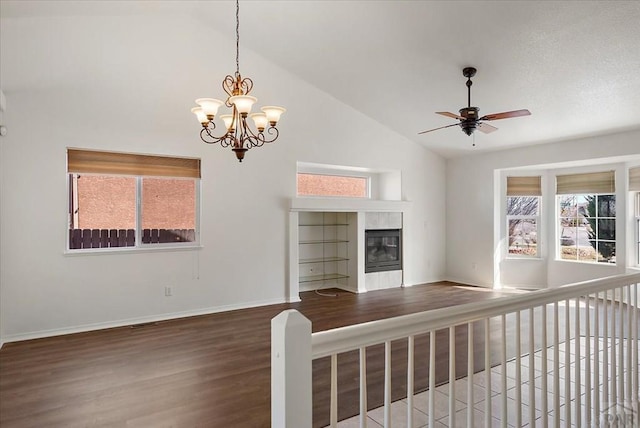 unfurnished living room with a tiled fireplace, ceiling fan with notable chandelier, wood finished floors, baseboards, and vaulted ceiling