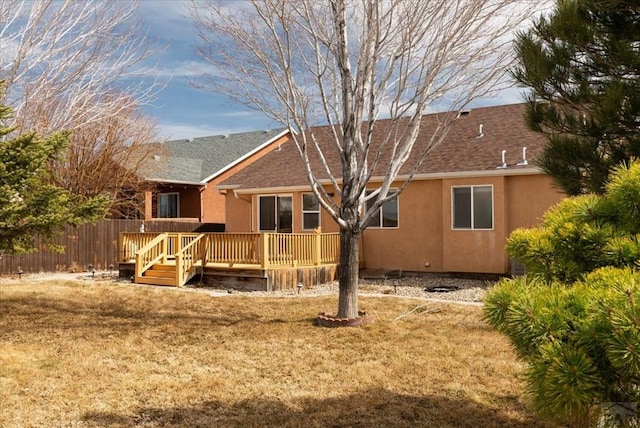 rear view of property with a shingled roof, fence, a wooden deck, stucco siding, and a yard