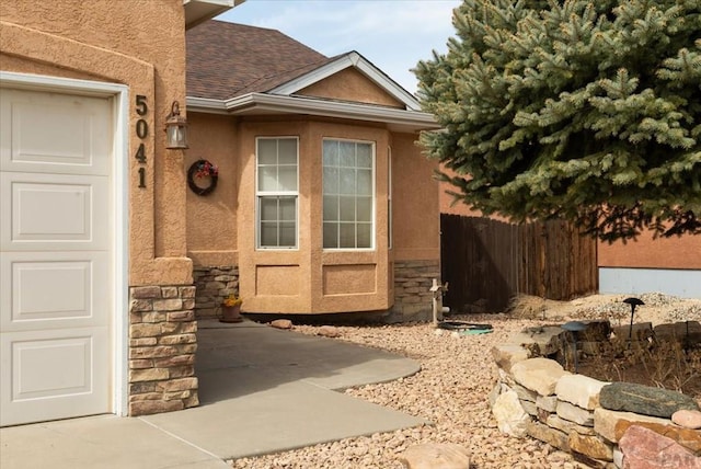 property entrance featuring a shingled roof, fence, stucco siding, a garage, and stone siding