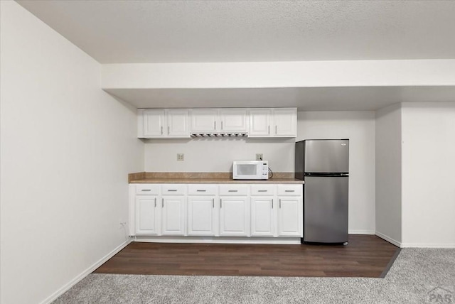 kitchen featuring white microwave, baseboards, freestanding refrigerator, white cabinetry, and dark colored carpet