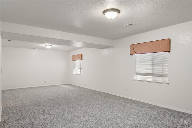 empty room with carpet flooring, baseboards, visible vents, and a textured ceiling