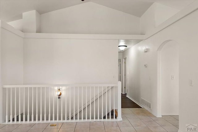 hall with light tile patterned floors, visible vents, arched walkways, and vaulted ceiling