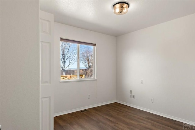 spare room with dark wood-type flooring, baseboards, and visible vents