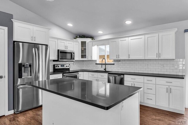 kitchen featuring stainless steel appliances, dark countertops, glass insert cabinets, white cabinets, and a sink