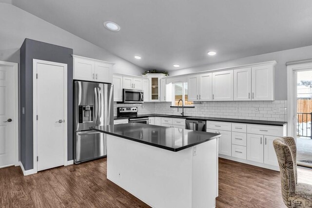 kitchen featuring stainless steel appliances, dark countertops, a sink, and white cabinetry