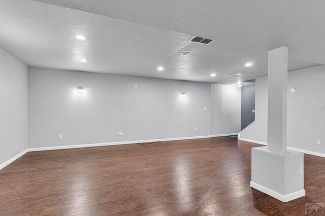 interior space featuring a textured ceiling, recessed lighting, visible vents, baseboards, and dark wood finished floors