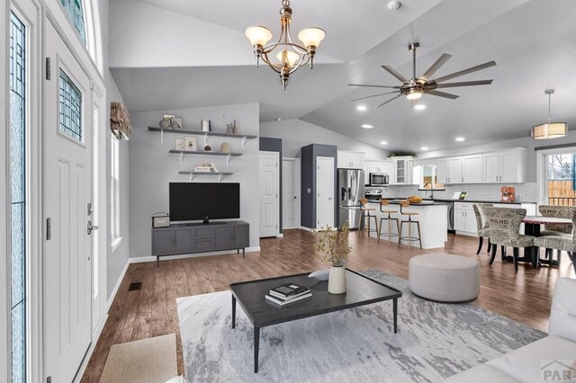 living room featuring lofted ceiling, recessed lighting, wood finished floors, baseboards, and ceiling fan with notable chandelier