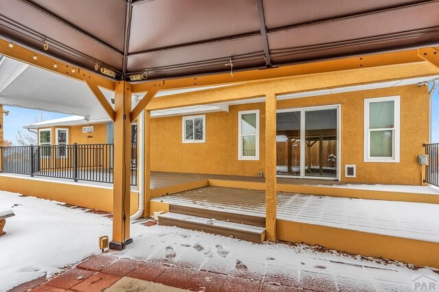 snow covered house featuring fence and stucco siding