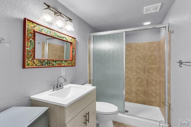 bathroom with a shower stall, vanity, visible vents, and a textured wall