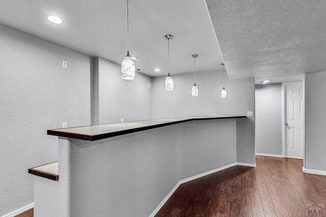 bar with recessed lighting, hanging light fixtures, dark wood-type flooring, a textured ceiling, and baseboards