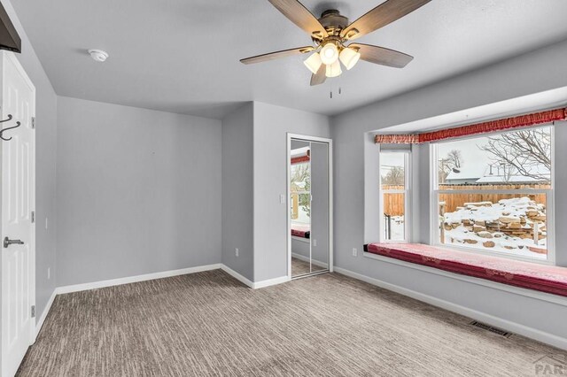 carpeted empty room with a ceiling fan, visible vents, and baseboards