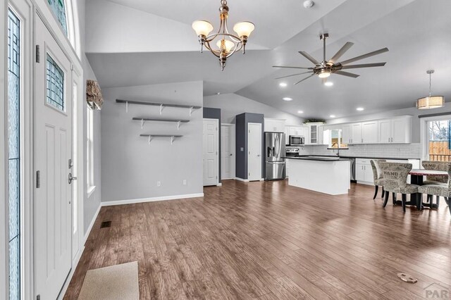 unfurnished living room featuring recessed lighting, ceiling fan with notable chandelier, baseboards, vaulted ceiling, and dark wood-style floors