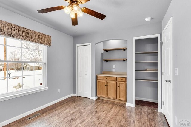 interior space featuring baseboards, visible vents, arched walkways, ceiling fan, and wood finished floors