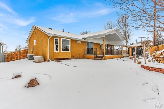 snow covered rear of property featuring covered porch, fence, and central AC