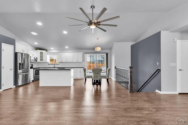 kitchen with lofted ceiling, white cabinetry, appliances with stainless steel finishes, dark countertops, and glass insert cabinets