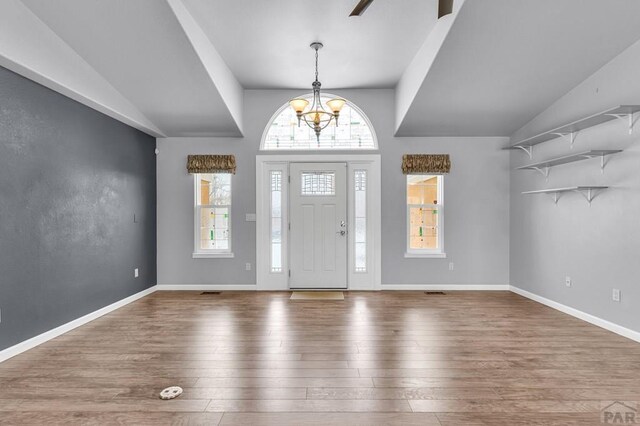 entryway with baseboards, a healthy amount of sunlight, an inviting chandelier, and wood finished floors