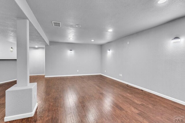 basement with baseboards, visible vents, dark wood-type flooring, a textured ceiling, and recessed lighting