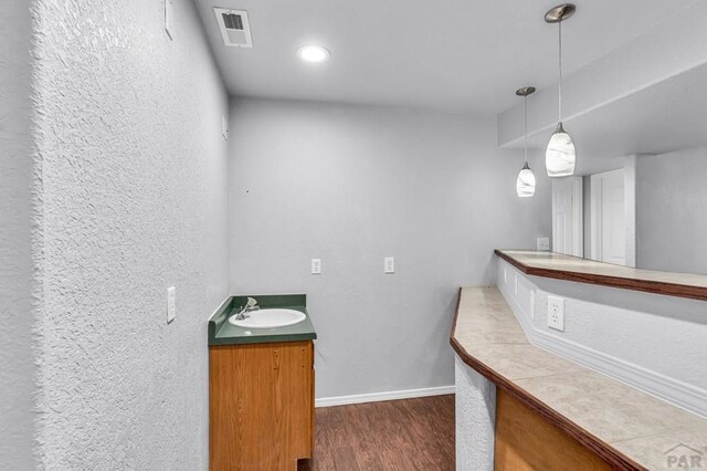 bathroom with a textured wall, wood finished floors, vanity, visible vents, and baseboards