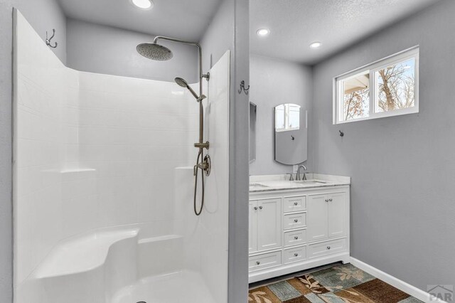 bathroom featuring double vanity, recessed lighting, a sink, baseboards, and walk in shower