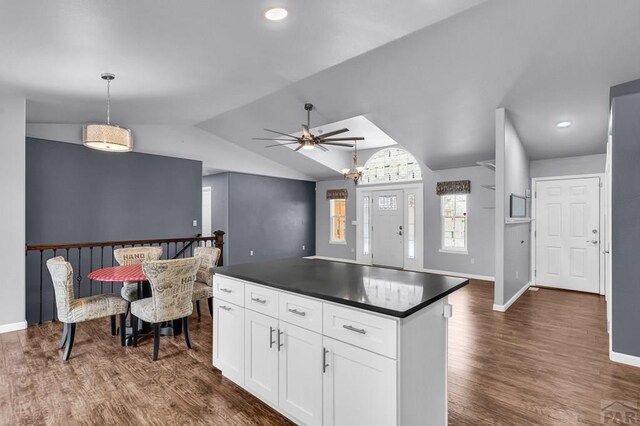 kitchen with lofted ceiling, white cabinetry, dark wood-style floors, dark countertops, and decorative light fixtures