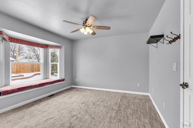 carpeted empty room featuring visible vents, a ceiling fan, and baseboards