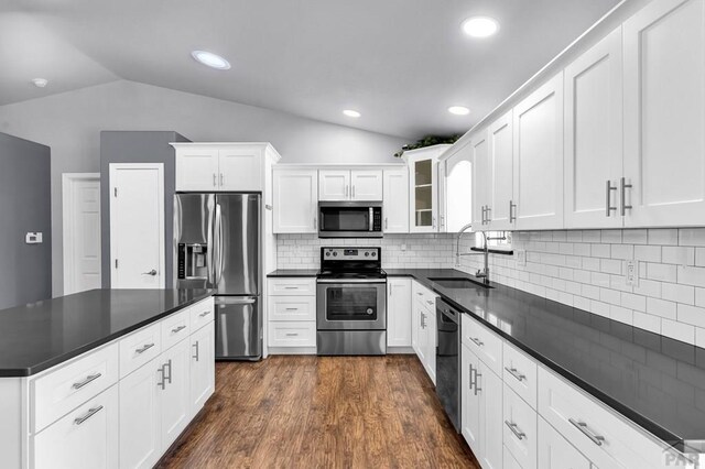 kitchen featuring dark countertops, appliances with stainless steel finishes, glass insert cabinets, white cabinets, and a sink